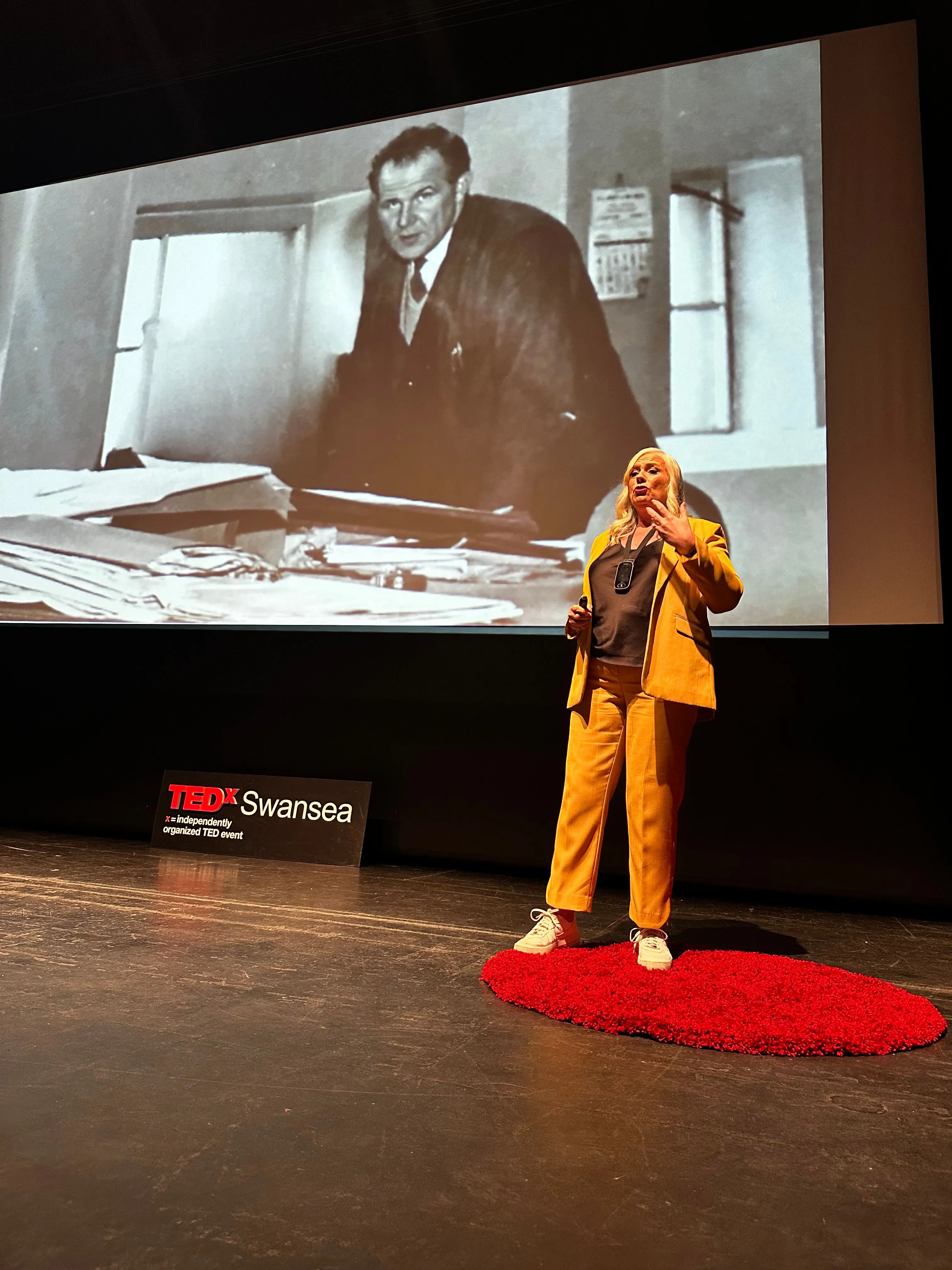 Alison speaking on the TEDx Swansea stage in an orange suit.