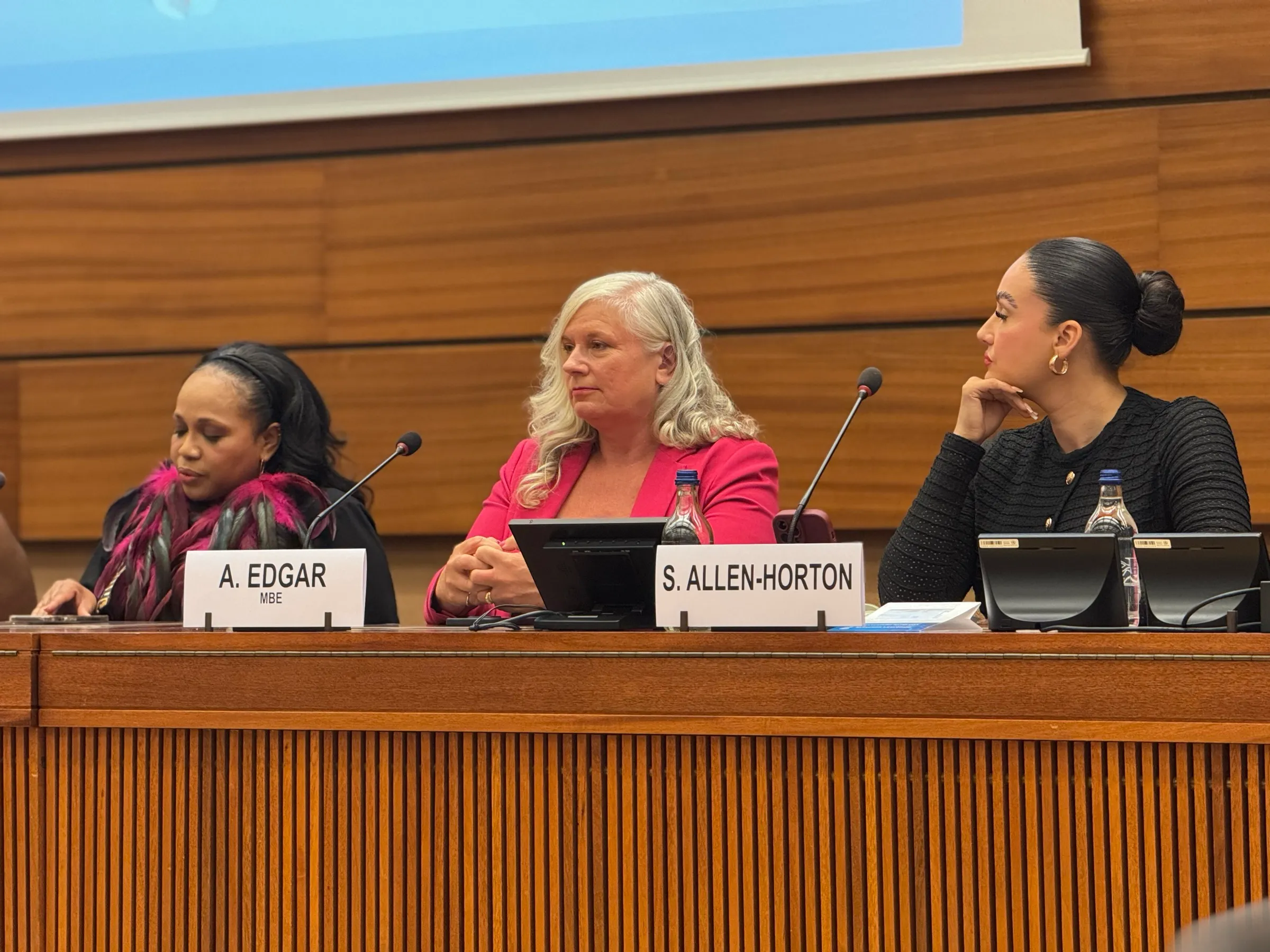 Alison on a United Nations panel, behind an A. Edgar MBE nameplate.
