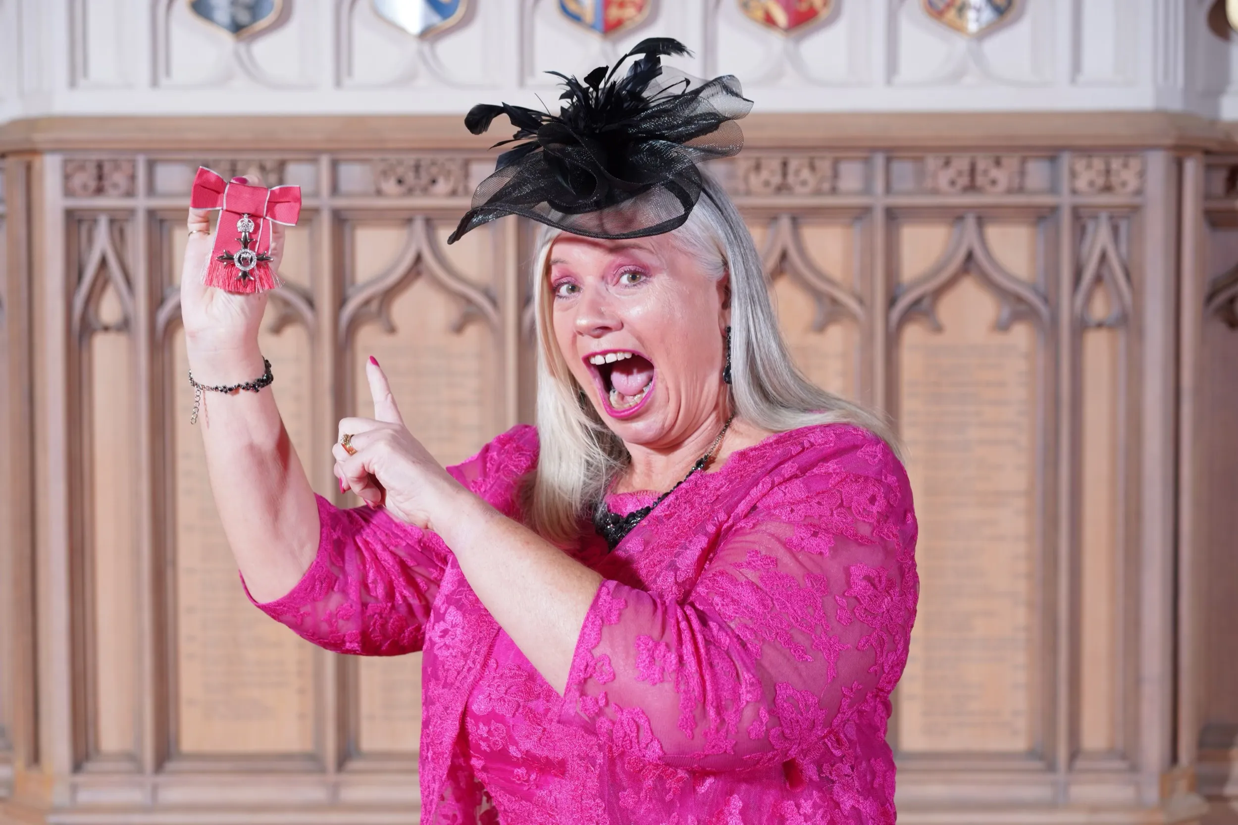 Alison at Windsor Castle in pink lace, delightedly pointing at her MBE.