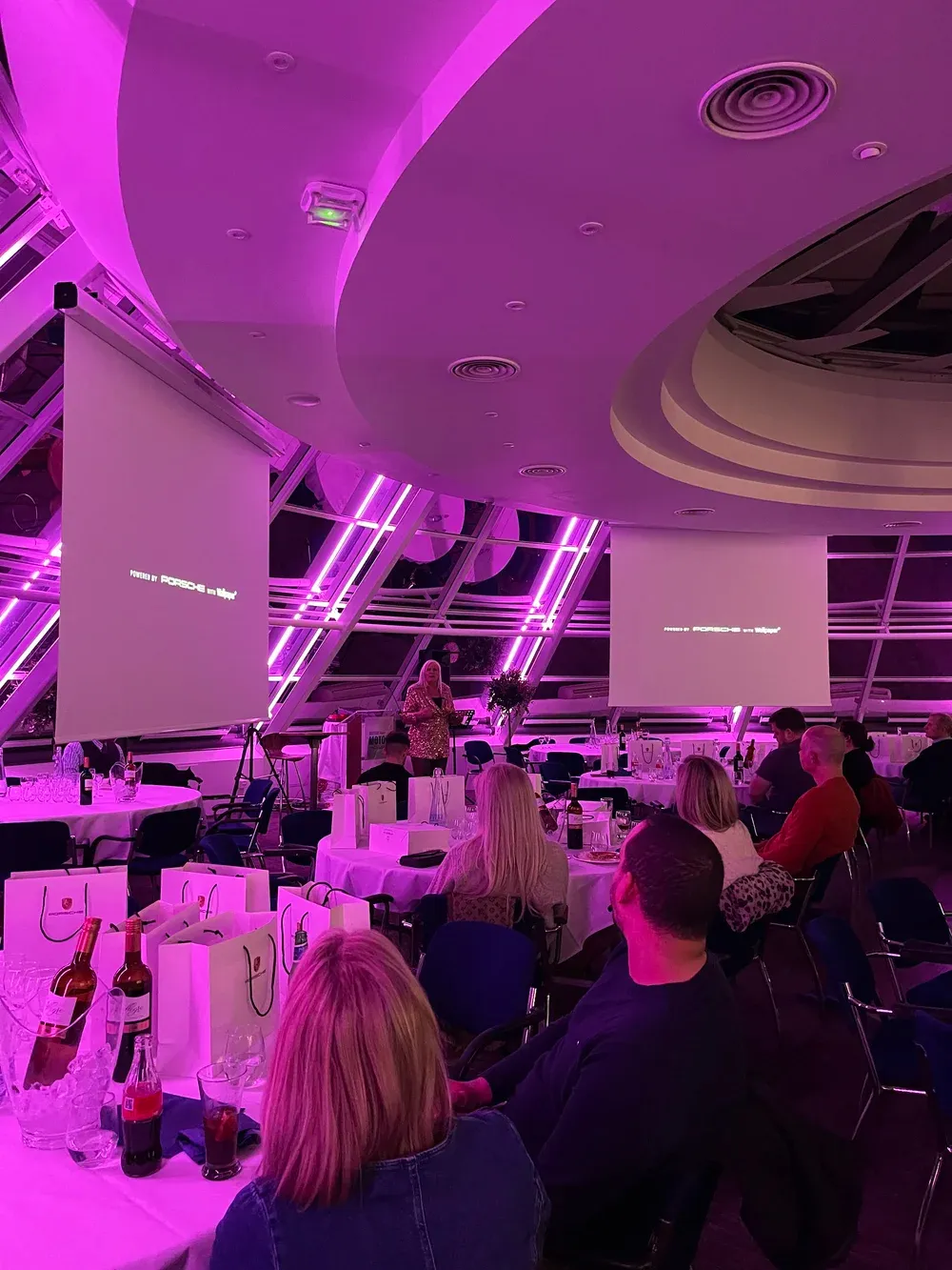 The Dare to Dream room mid-keynote, Porsche on the screens and gift bags on the tables, Alison speaking at the front.