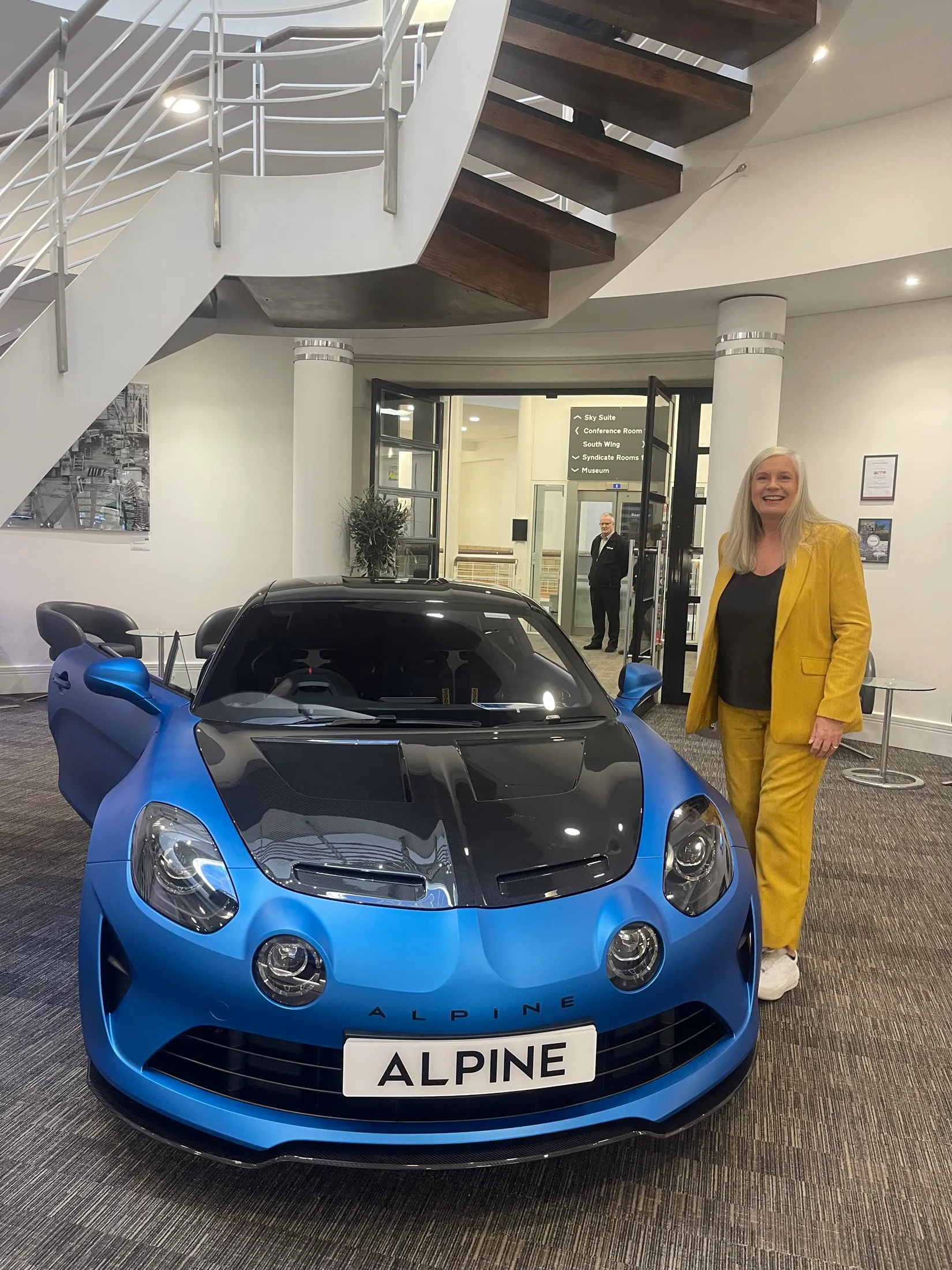 Alison beside a blue Alpine sports car at the British Motor Museum.